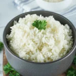 A single serving of cooked white rice garnished with a sprig of parsley on a kitchen counter.