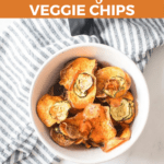 Bowl of homemade air fryer veggie chips placed on a white and gray striped cloth, with text overlay "Air Fryer Veggie Chips.