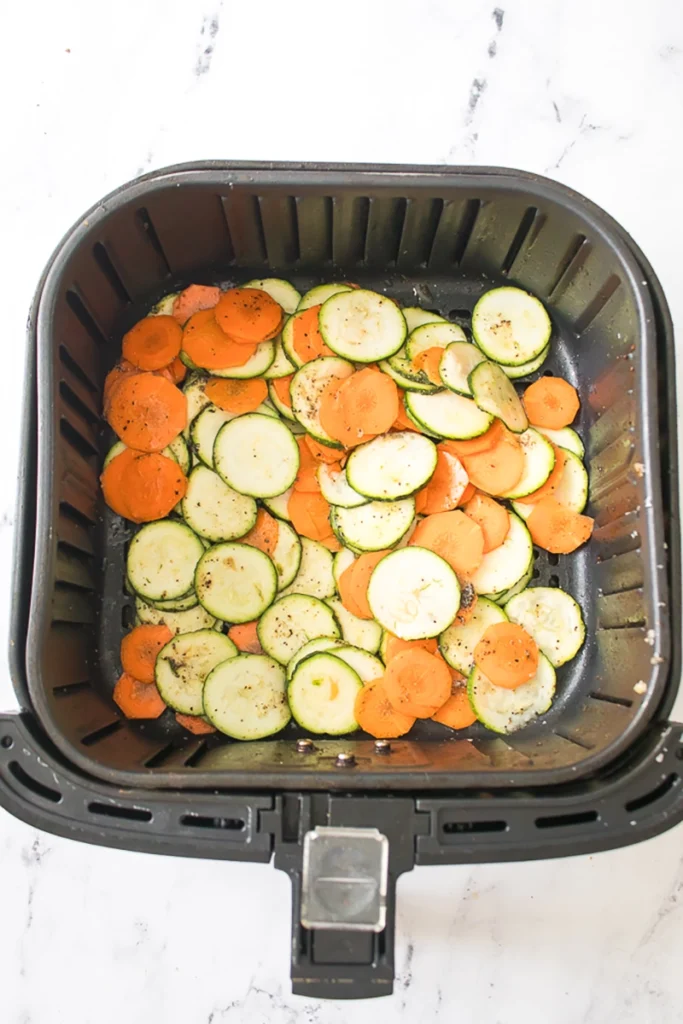 Slices of zucchini and carrots seasoned with herbs inside an air fryer basket.