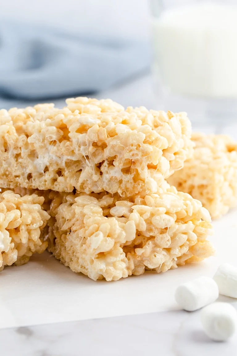 Stack of homemade small batch Rice Krispies treats on a white surface, with a glass of milk and marshmallows in the background.