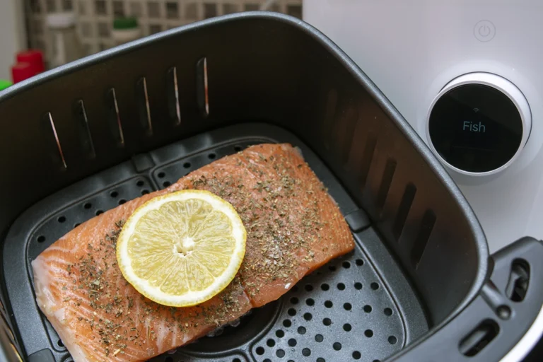 A salmon fillet with seasoning and a lemon slice on top is placed inside an air fryer for one person, with the air fryer display reading "Fish.