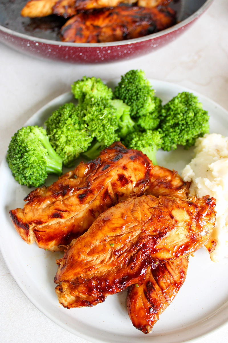 A plate featuring honey mustard chicken tenders served alongside steamed broccoli and creamy mashed potatoes.