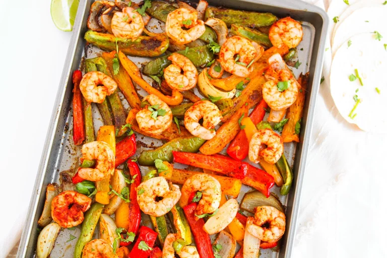 Sheet pan with cooked shrimp, sliced bell peppers, and onions, garnished with herbs. Perfect for sheetpan shrimp fajitas—just scoop into tortillas and add a squeeze of lime for an easy dinner on one pan.
