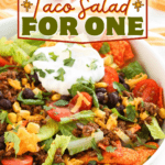 A bowl of doritos taco salad for one, topped with crisp lettuce, seasoned ground beef, melty cheese, hearty black beans, sweet corn, fresh tomatoes, and a dollop of sour cream. Text reads: “Doritos Taco Salad For One.”.