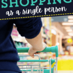 A person is pushing a shopping cart down a grocery store aisle with text overlay that reads “Grocery shopping for one as a single person.”.