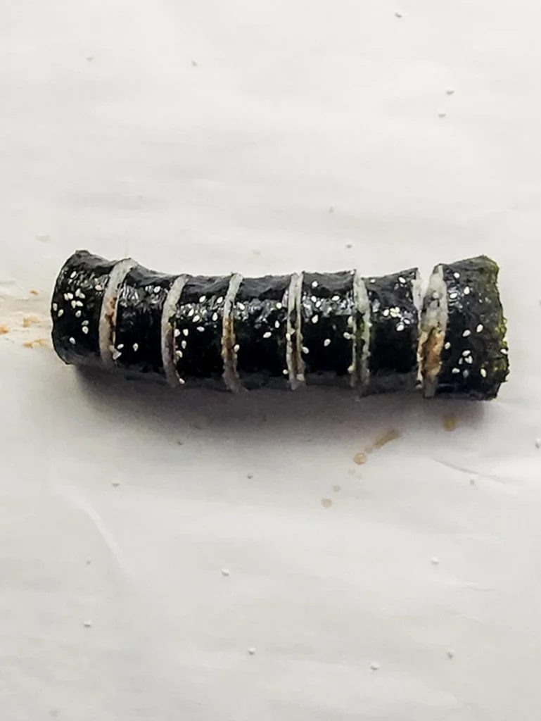 A sliced spicy tuna kimbap roll wrapped in seaweed is placed on a white surface.