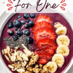 A single serving acai bowl, viewed from above, topped with blueberries, sliced strawberries, banana, chia seeds, almond slices, and granola.