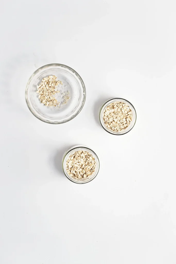 Three glass bowls of peanut butter and jelly overnight oats are arranged on a white surface, with one larger bowl at the top left and two smaller bowls below it.