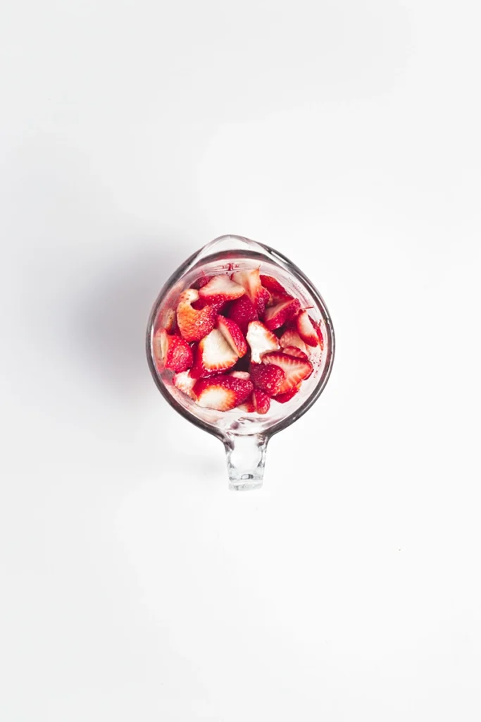 A glass measuring cup filled with sliced strawberries, viewed from above on a white background—perfect for topping peanut butter and jelly overnight oats.