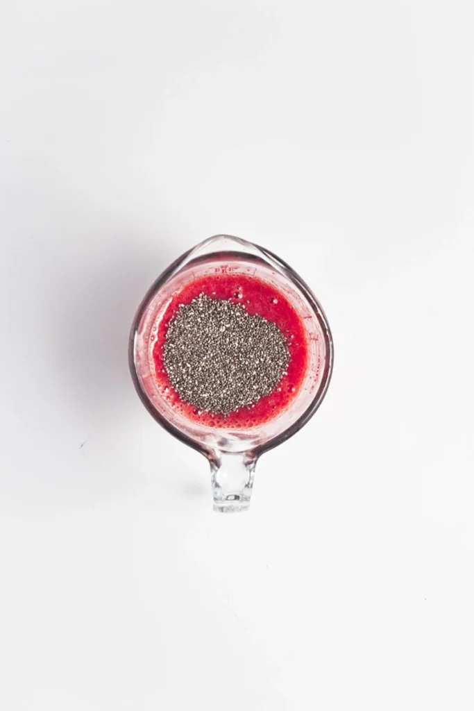 A glass measuring cup filled with a red liquid topped with a layer of chia seeds, photographed from above on a white background—perfect for making peanut butter and jelly overnight oats.
