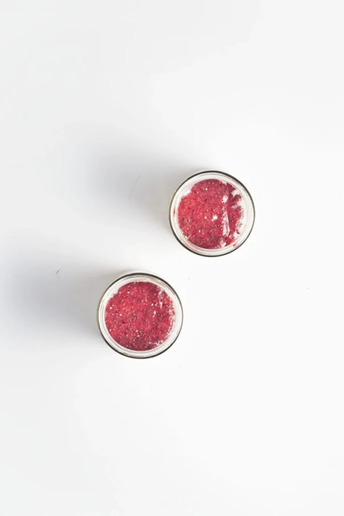 Two small glass jars filled with red jam or fruit puree are placed on a white surface, perfect for adding to peanut butter and jelly overnight oats for a delicious breakfast treat.