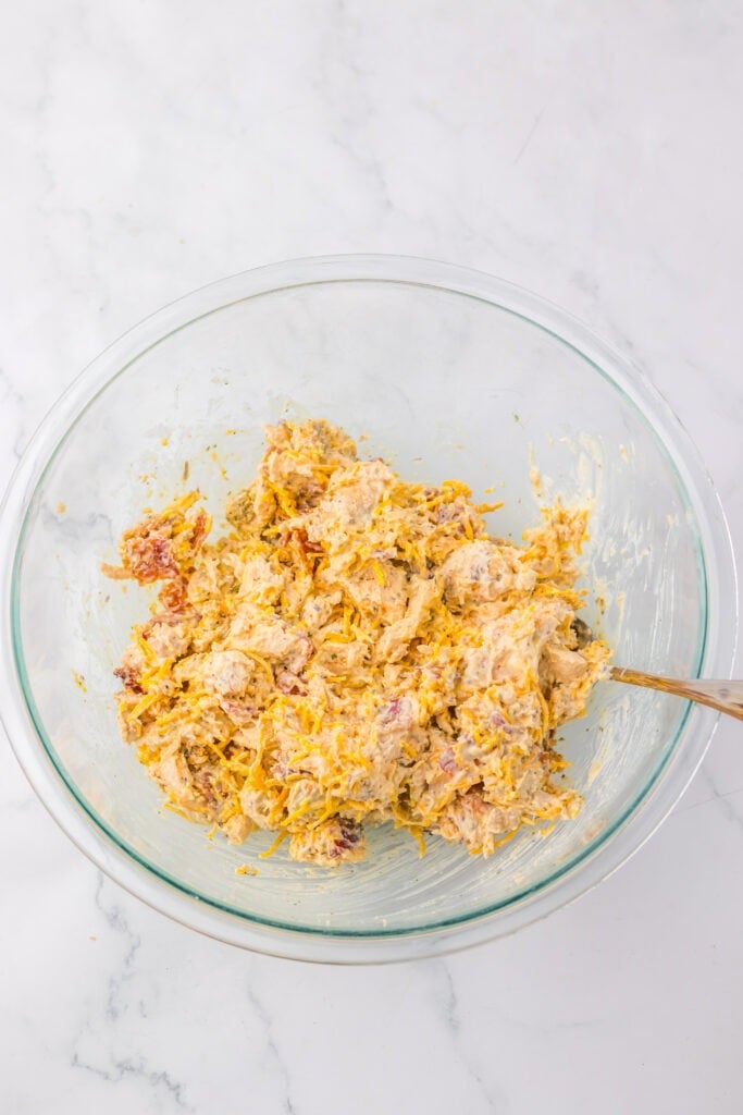 A glass bowl filled with a creamy, mixed chicken salad containing shredded chicken, spices, and visible pieces of vegetables—reminiscent of the popular Chicken Salad Chick Sassy Scotty chicken salad.