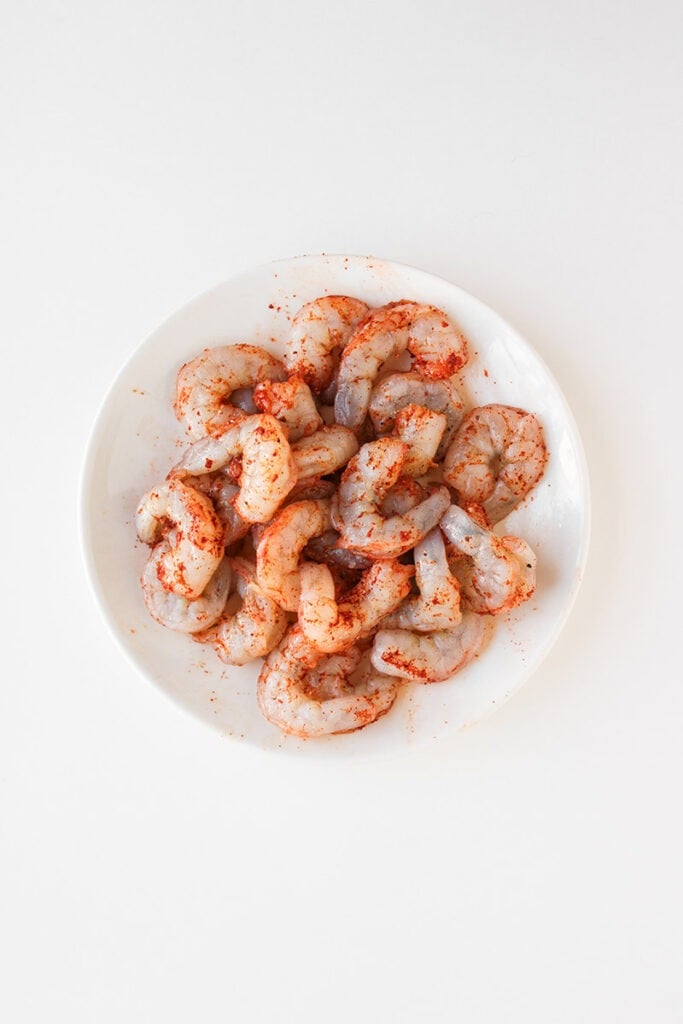 Raw shrimp seasoned with red spices arranged on a white plate, photographed from above against a plain white background—perfect as a fresh base for your next bang bang shrimp bowl or creative shrimp bowl recipe.