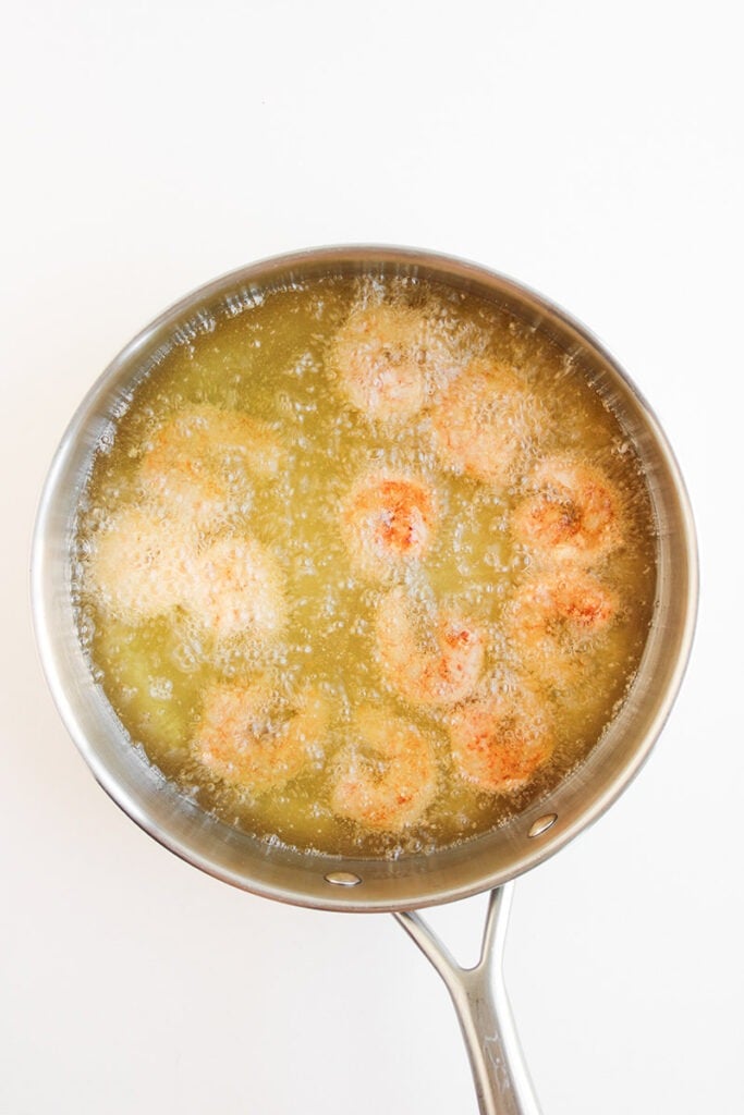 Raw shrimp are being deep-fried in hot oil in a stainless steel pan, with visible bubbling around the shrimp pieces—an essential first step for any delicious shrimp bowl recipe or flavorful bang bang shrimp bowl.