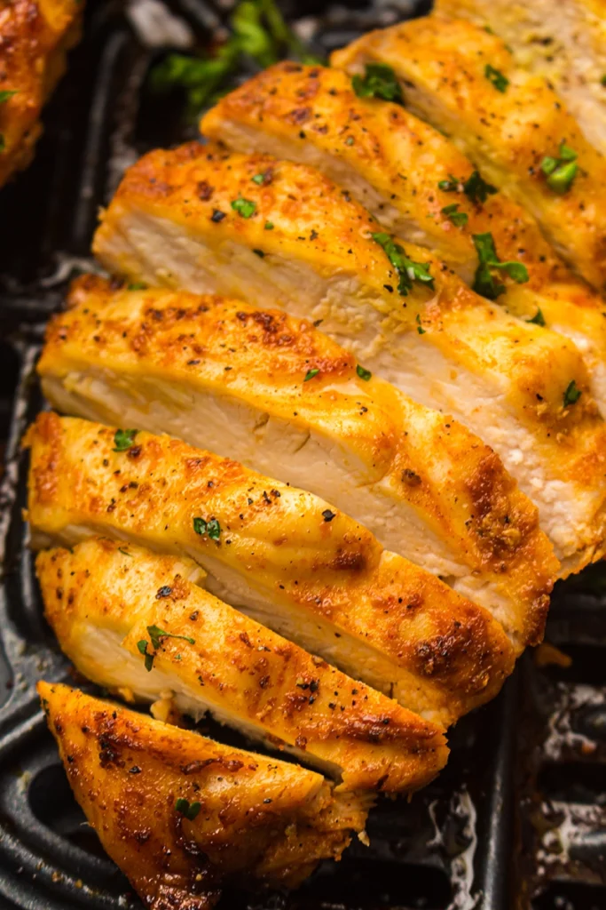 Sliced air fryer chicken breast seasoned with herbs and spices, cooked to perfection with visible grill marks and garnished with chopped parsley.
