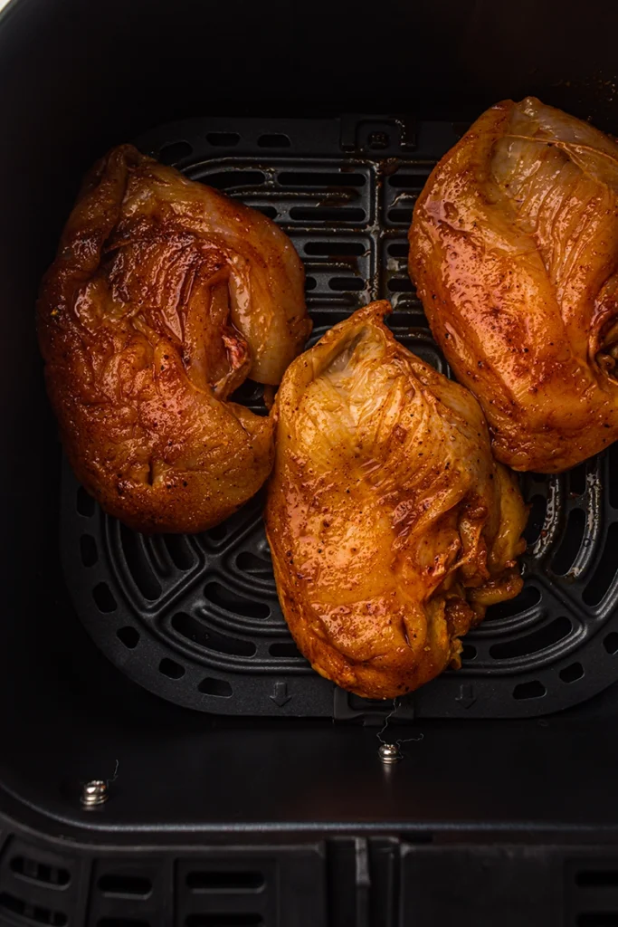 Three seasoned chicken thighs cooking inside an air fryer basket, showcasing the delicious results you can achieve with air fryer chicken.