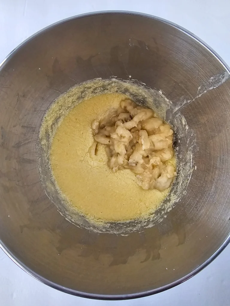 A metal mixing bowl containing a yellow batter with mashed bananas added on top, ready to be mixed together for a small batch banana bread.