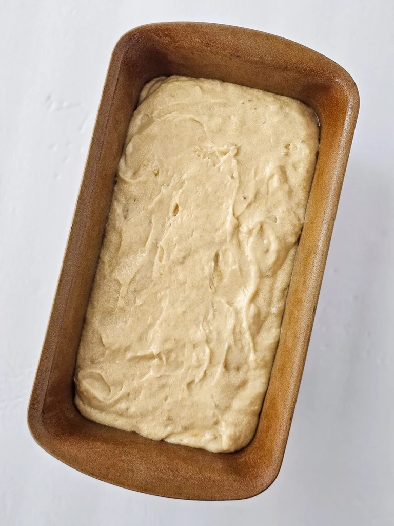 A loaf pan filled with unbaked small batch banana bread batter sits on a white surface, ready to be placed in the oven.
